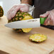 A person using a Dexter-Russell green chef knife to cut a pineapple on a counter.