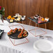 An Acopa Slate Rose Gold Wire Riser set on a table with plates of food.