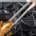 A hand using Vollrath VersaGrip tongs to cook chicken in a pan.