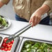 A person using Vollrath stainless steel utility tongs to serve vegetables.