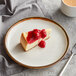 An Acopa Keystone vanilla bean stoneware coupe plate with a slice of cheesecake topped with red sauce.