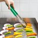 A hand using Vollrath Jacob's Pride tongs with green coated Kool Touch handles to serve vegetables.