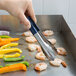 A hand holding Vollrath Jacob's Pride tongs with blue Kool Touch handles over a pan of shrimp.