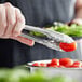 A person using Vollrath stainless steel utility tongs to hold a cherry tomato.