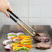 Vollrath Jacob's Pride tongs with assorted colors Kool Touch handles cooking meat and vegetables on a grill.