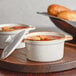 Two Acopa Keystone vanilla bean stoneware mini casserole dishes with lids filled with soup on a tray.