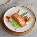 A Acopa Keystone stoneware coupe plate with salmon and asparagus on a table with a glass of wine.