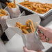 A hand using the right handle of a Vollrath Plastic FryBagger to scoop french fries into a bag.
