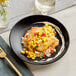 A plate of fish with mango salsa and rice on an Acopa matte black stoneware coupe plate with a fork.