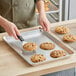 A person putting chocolate chip cookies on a Choice aluminum sheet pan.