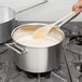 A person stirring a Vollrath stainless steel sauce pan with a wooden spoon.