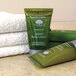 A group of green Basic Earth Botanicals body lotion bottles next to a stack of white towels.