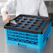 A chef using a Cambro black plastic ice scoop to fill blue plastic glass racks.