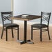 A Lancaster Table & Seating butcher block table with espresso finish and cast iron base plate and two black chairs with cushions.