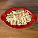 A red Fiesta oval casserole dish filled with pasta and vegetables.