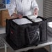 A chef in a white shirt holding a black Cambro delivery bag filled with food containers.