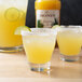 A group of glasses of yellow Monin margaritas with lime slices on the rim.
