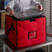 A chef putting a tray of food in a red Cambro GoBag.