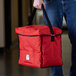 A person holding a red Cambro insulated top loading GoBag with black straps.