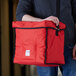 A man holding a red Cambro insulated GoBag with a handle.