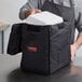 A person putting a white food container into a black Cambro GoBag.