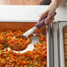 A person using a Vollrath purple handle portion spoon to scoop vegetables into a bowl.