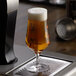 A Stolzle stemmed beer glass full of beer on a bar counter.