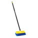 A blue and yellow Rubbermaid bi-level floor scrub brush with a handle.