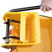 A person using a yellow Lavex side press wringer on a yellow mop bucket.