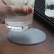 A hand holding a glass of water on a customizable silver vinyl coaster on a table.