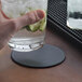 A hand holding a glass of water with cucumbers on a customizable black vinyl coaster.