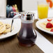 A Tablecraft syrup dispenser with a chrome lid on a table with waffles and orange juice.
