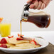 A person using a Tablecraft Polypropylene Teardrop Syrup Dispenser to pour syrup on pancakes and strawberries.