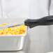 The handle of a Vollrath Jacob's Pride Black Solid Oval Spoodle sticking out of a pan of corn.
