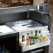 A Carlisle portable bar with a cherry wood counter and a black lid on a sink.