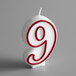 A white and red candle with a red outlined number 9 on it.
