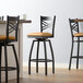 A group of three Lancaster Table & Seating black swivel bar stools with light brown vinyl padded seats at a table.