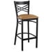 A Lancaster Table & Seating black cross back bar stool with a light brown cushion on the seat.