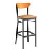 A Lancaster Table & Seating black bar stool with a light brown cushion and cherry wood back.