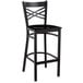 A black metal Lancaster Table & Seating cross back bar stool with a black wood seat.