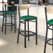 A Lancaster Table & Seating black bar stool with green vinyl seat and driftwood back.