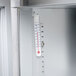 A thermometer on a metal shelf inside a Traulsen sandwich prep table.