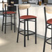 A Lancaster Table & Seating Boomerang bar stool with a red vinyl seat and driftwood back.