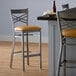 A Lancaster Table & Seating cross back bar stool with a light brown cushion on a table.