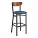 A Lancaster Table & Seating black bar stool with a navy vinyl seat and a wood back.