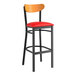 A black Lancaster Table & Seating bar stool with red vinyl seat and cherry wood back.