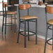 Lancaster Table & Seating Boomerang Series bar stools with light brown vinyl seats and antique walnut wood backs at a restaurant counter.