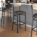 A group of Lancaster Table & Seating black bar stools with driftwood backs and dark brown vinyl seats at a counter.
