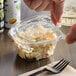A hand using a fork to open a Dart ClearPac plastic container of food on a table in a salad bar.