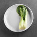 A white Elite Global Solutions round melamine plate with a vegetable on it.